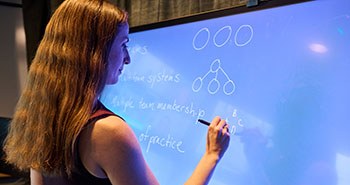 An instructor writes on a wall-size tablet, dynamically diagramming concepts and adding markup to documents for enhanced learning.