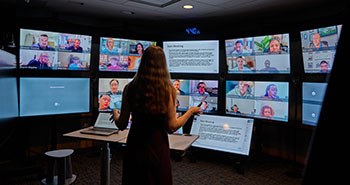 A view from within the learning studio room, looking over the instructor's shoulder at a display showing live feeds of all of the students. Each learner is visible to the instructor as clearly as if they were in the room.